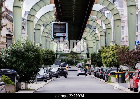 Wuppertal, Deutschland. September 2024. Oberhalb der Sonnborner Straße verläuft eine Schwebebahn. Laut Marco Polo Trendguide`25 entwickelt sich die Stadt im Bergischen Land derzeit zu einer Art Kunsthochburg: „Wenn man in Wuppertal unterwegs ist, glaubt man seinen Augen nicht. Hyper-realistische, poetische, surreale und abstrakte Wandmalereien prangen meterhoch an den Fassaden.“ Sie sind Teil des Projekts Urbaner Kunstraum Wuppertal (UKW), das bis Ende 2025 mit 24 großformatigen Gemälden Farbe in die Stadtteile bringen wird. Quelle: Rolf Vennenbe/dpa/Alamy Live News Stockfoto